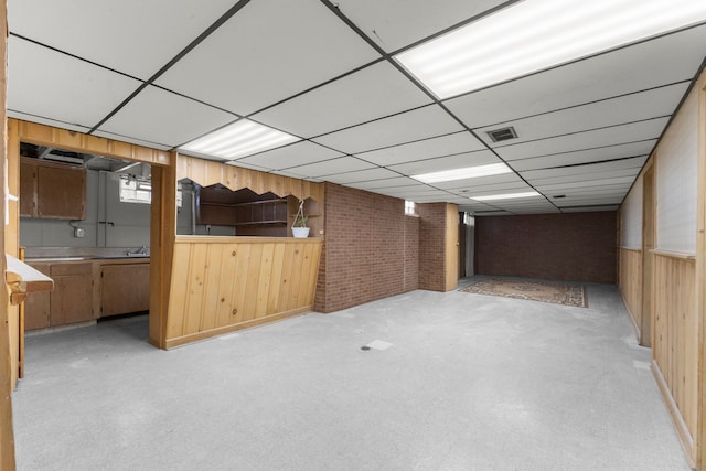 basement featuring wooden walls, brick wall, and a paneled ceiling