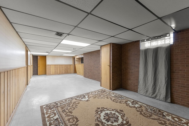 basement featuring brick wall, a drop ceiling, and wooden walls