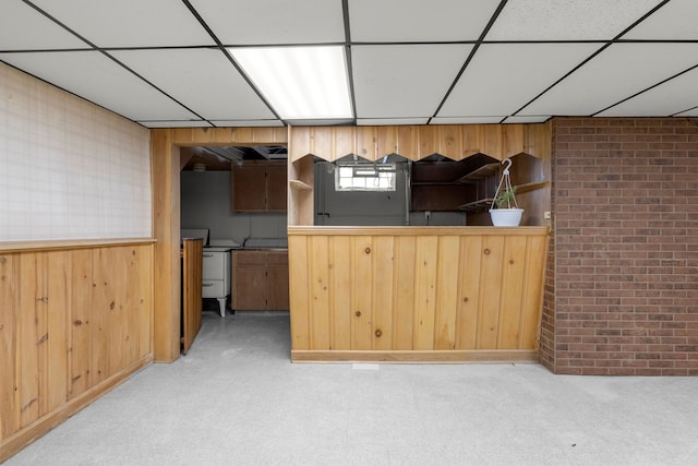 kitchen featuring a paneled ceiling, brick wall, wooden walls, and carpet flooring