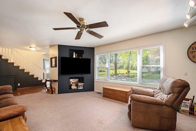 living room with a large fireplace, ceiling fan, and carpet flooring