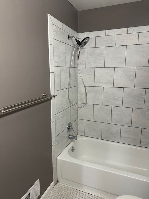 bathroom with toilet, tiled shower / bath combo, and tile patterned flooring