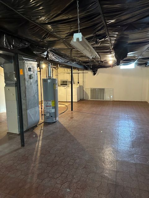 basement featuring heating unit, washer and clothes dryer, and water heater