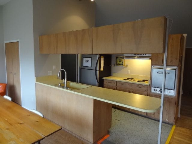 kitchen with black refrigerator, sink, high vaulted ceiling, and kitchen peninsula