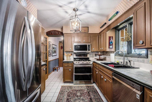 kitchen featuring sink, light tile patterned floors, appliances with stainless steel finishes, a notable chandelier, and pendant lighting