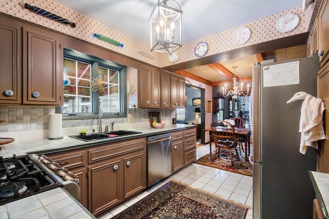 kitchen featuring sink, appliances with stainless steel finishes, tile counters, a notable chandelier, and pendant lighting