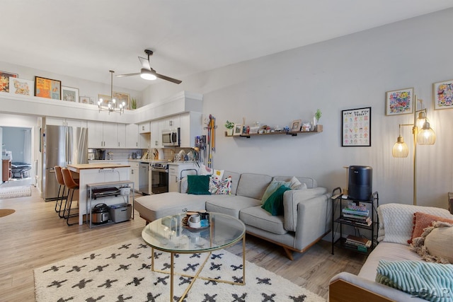 living room featuring ceiling fan with notable chandelier and light wood-type flooring