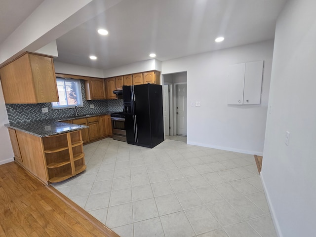 kitchen featuring black fridge with ice dispenser, sink, dark stone countertops, stainless steel range, and decorative backsplash