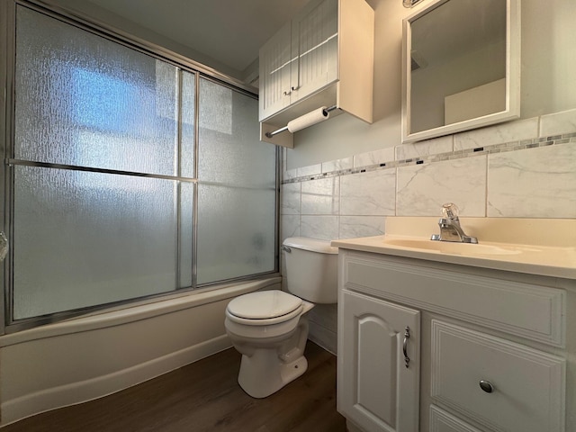 full bathroom with tile walls, bath / shower combo with glass door, vanity, wood-type flooring, and toilet