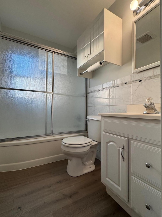 full bathroom with toilet, tile walls, vanity, hardwood / wood-style flooring, and enclosed tub / shower combo