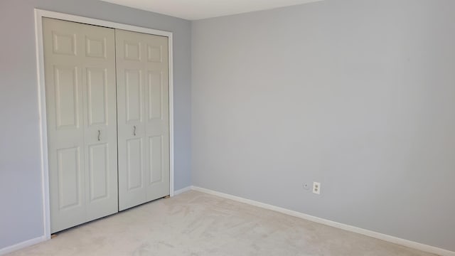 unfurnished bedroom featuring light carpet, baseboards, and a closet
