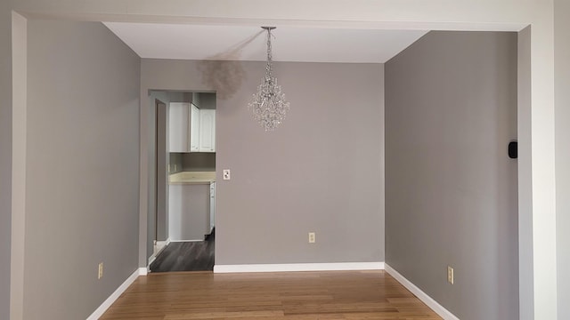 unfurnished dining area with wood finished floors, baseboards, and a chandelier