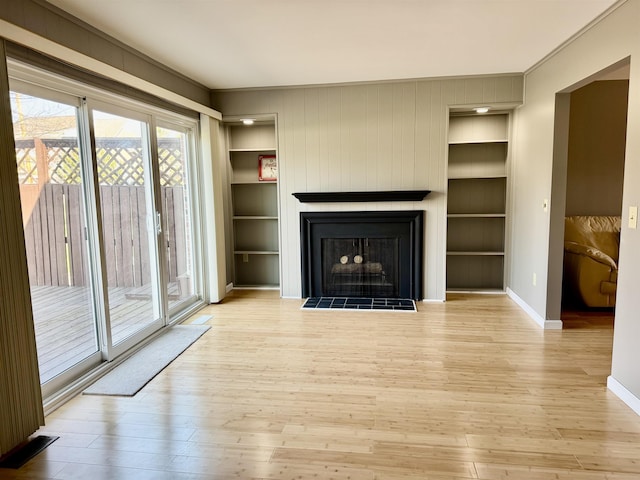 unfurnished living room with built in shelves, wood finished floors, and baseboards