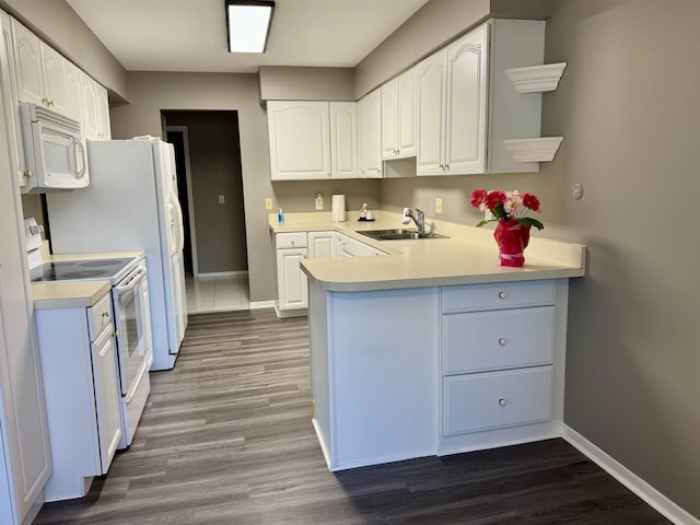 kitchen featuring white appliances, a peninsula, a sink, and baseboards