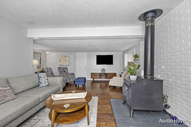 living room featuring dark wood-type flooring, brick wall, a textured ceiling, and a wood stove