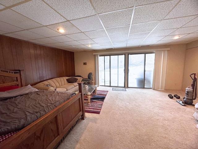 carpeted bedroom with access to outside, a drop ceiling, and wooden walls