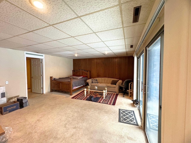 living room with a paneled ceiling, wooden walls, and carpet