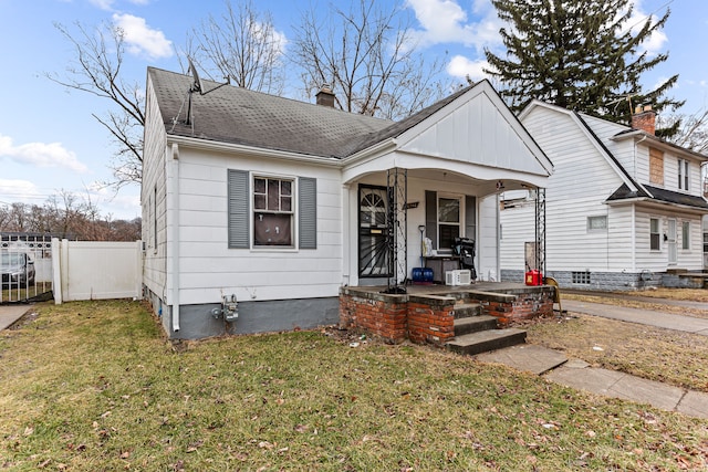 bungalow-style home featuring a shingled roof, a chimney, a porch, fence, and a front lawn