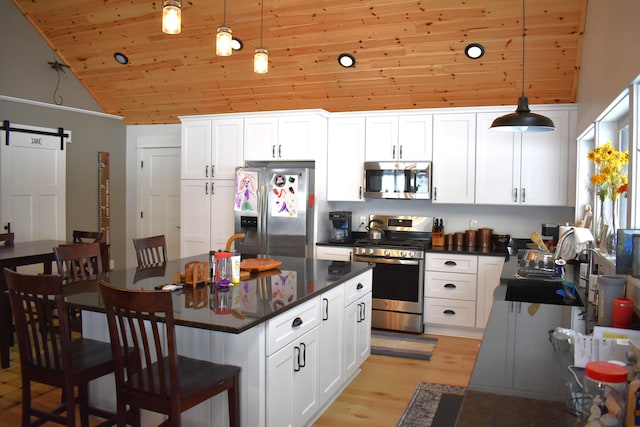 kitchen with a kitchen island, white cabinetry, hanging light fixtures, stainless steel appliances, and a barn door