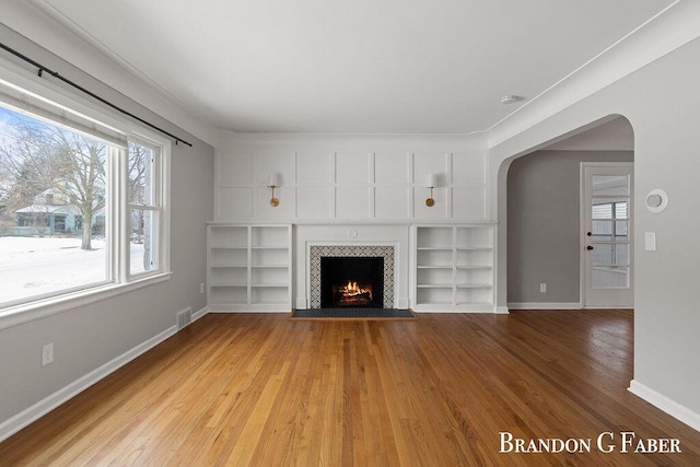 unfurnished living room featuring built in shelves, a tile fireplace, and light hardwood / wood-style flooring