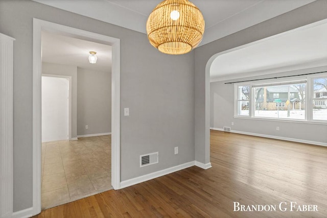 empty room featuring wood-type flooring and a chandelier