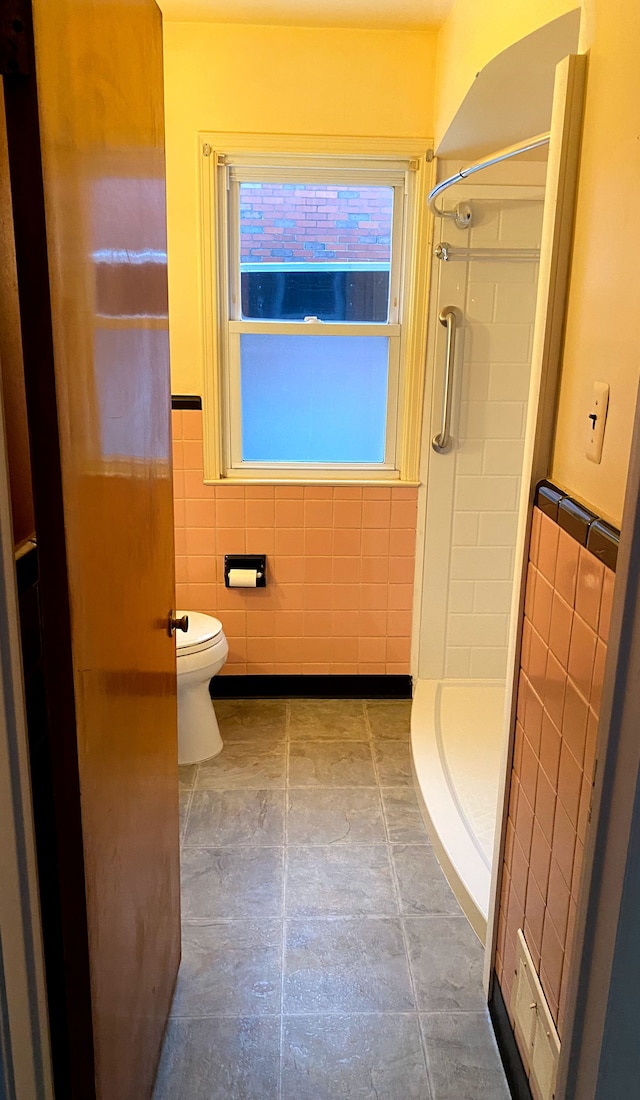 bathroom featuring tiled shower, toilet, and tile walls