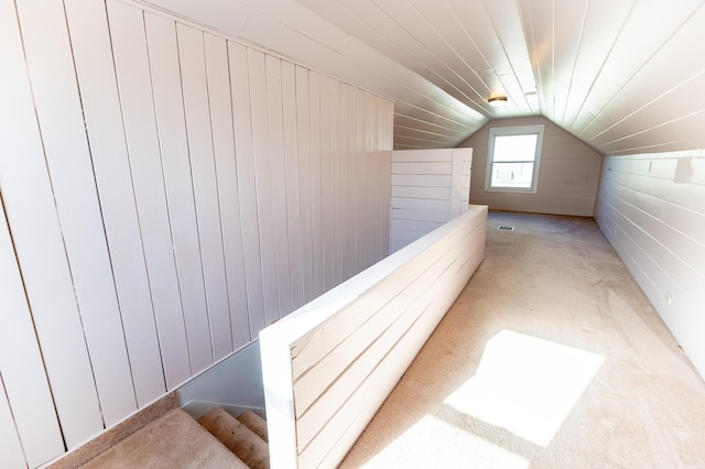 interior space with vaulted ceiling, light carpet, and wood walls