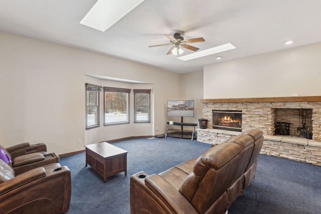 living room featuring ceiling fan, a stone fireplace, a skylight, and dark colored carpet