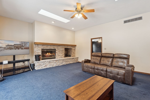 living room featuring ceiling fan, a fireplace, a skylight, and dark carpet