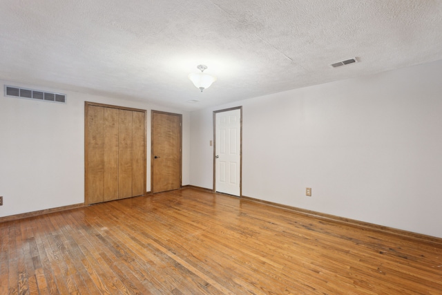 unfurnished bedroom with hardwood / wood-style floors, a textured ceiling, and two closets