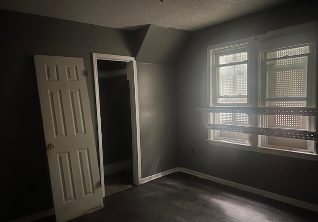 unfurnished bedroom featuring dark hardwood / wood-style flooring, lofted ceiling, a textured ceiling, and a closet