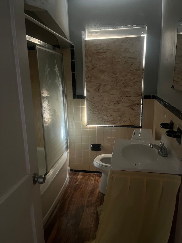 full bathroom featuring combined bath / shower with glass door, tile walls, hardwood / wood-style flooring, vanity, and toilet