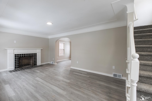 unfurnished living room featuring a tiled fireplace, crown molding, and hardwood / wood-style floors