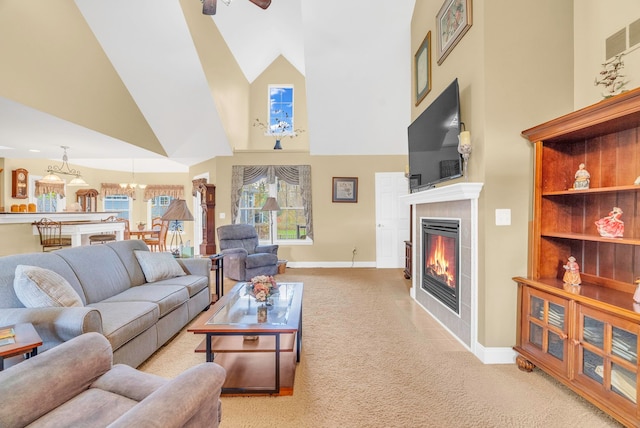 carpeted living room with a fireplace, ceiling fan with notable chandelier, and a high ceiling