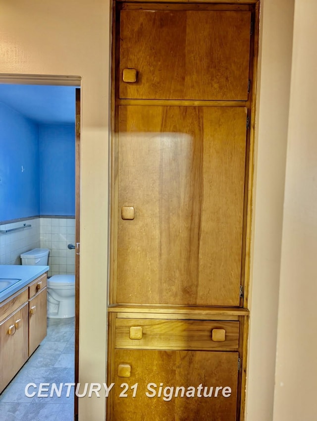 bathroom with wainscoting, vanity, toilet, and tile walls