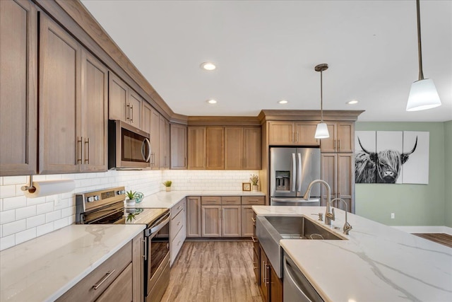 kitchen with a sink, pendant lighting, light wood-style floors, and stainless steel appliances