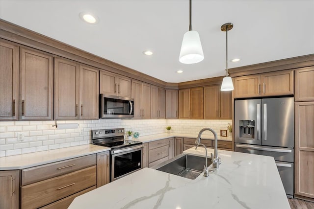 kitchen featuring light stone countertops, a sink, appliances with stainless steel finishes, pendant lighting, and tasteful backsplash