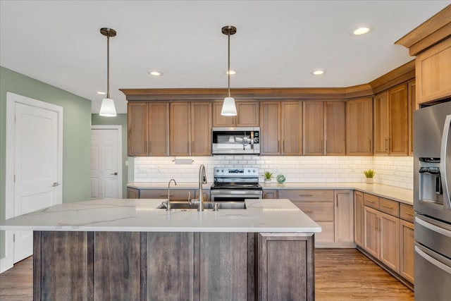 kitchen featuring a sink, light stone countertops, light wood-style flooring, stainless steel appliances, and a kitchen island with sink