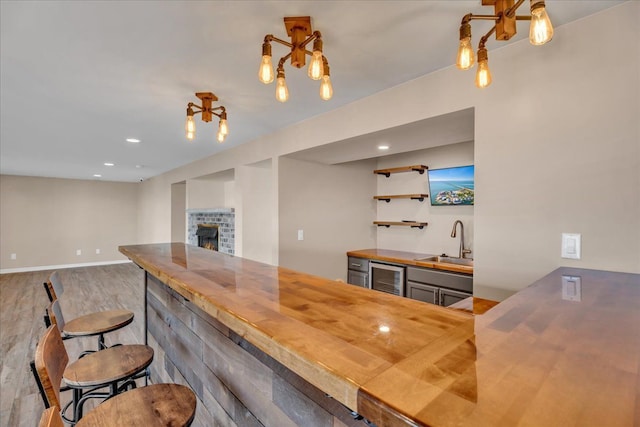 kitchen with a sink, wood counters, a warm lit fireplace, wood finished floors, and wine cooler