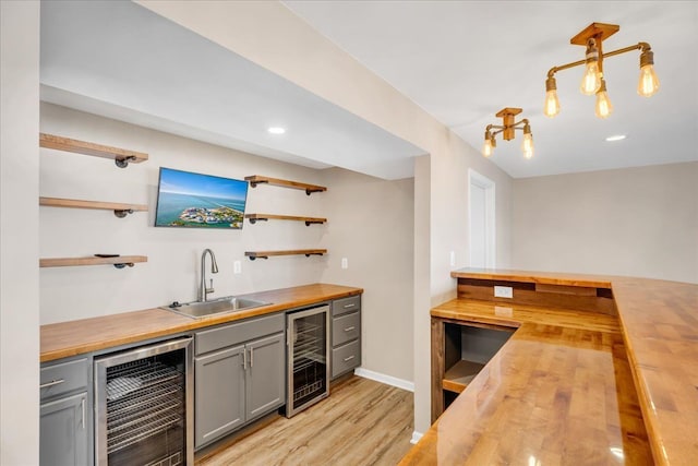 bar with beverage cooler, light wood-style flooring, wet bar, and a sink