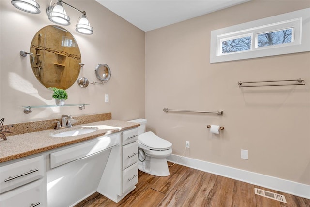 bathroom featuring visible vents, toilet, wood finished floors, baseboards, and vanity