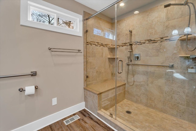 bathroom featuring wood finished floors, baseboards, visible vents, plenty of natural light, and a shower stall