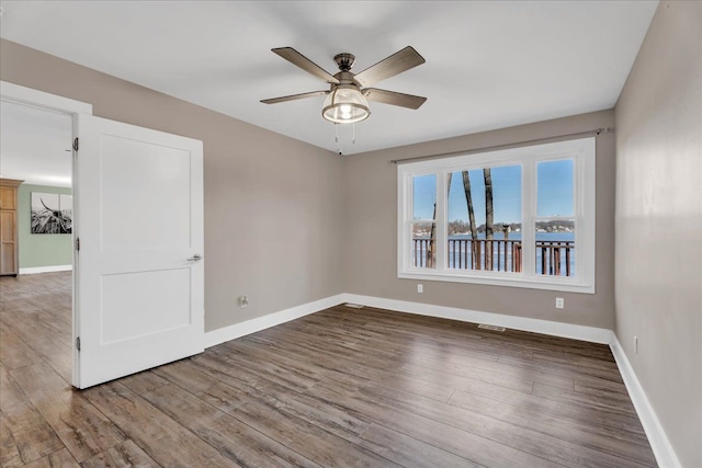 empty room featuring ceiling fan, visible vents, baseboards, and wood finished floors