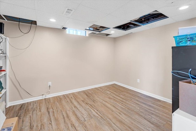 below grade area featuring visible vents, baseboards, recessed lighting, a drop ceiling, and light wood-style floors