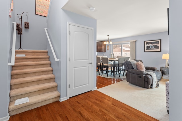 stairs with wood-type flooring and a notable chandelier