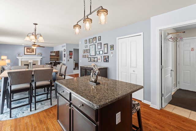 kitchen featuring dark brown cabinetry, a center island, hanging light fixtures, dark stone counters, and light hardwood / wood-style floors