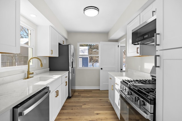 kitchen with appliances with stainless steel finishes, a wealth of natural light, white cabinetry, light hardwood / wood-style floors, and light stone countertops