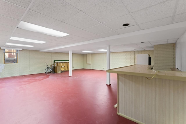 basement featuring brick wall and a paneled ceiling