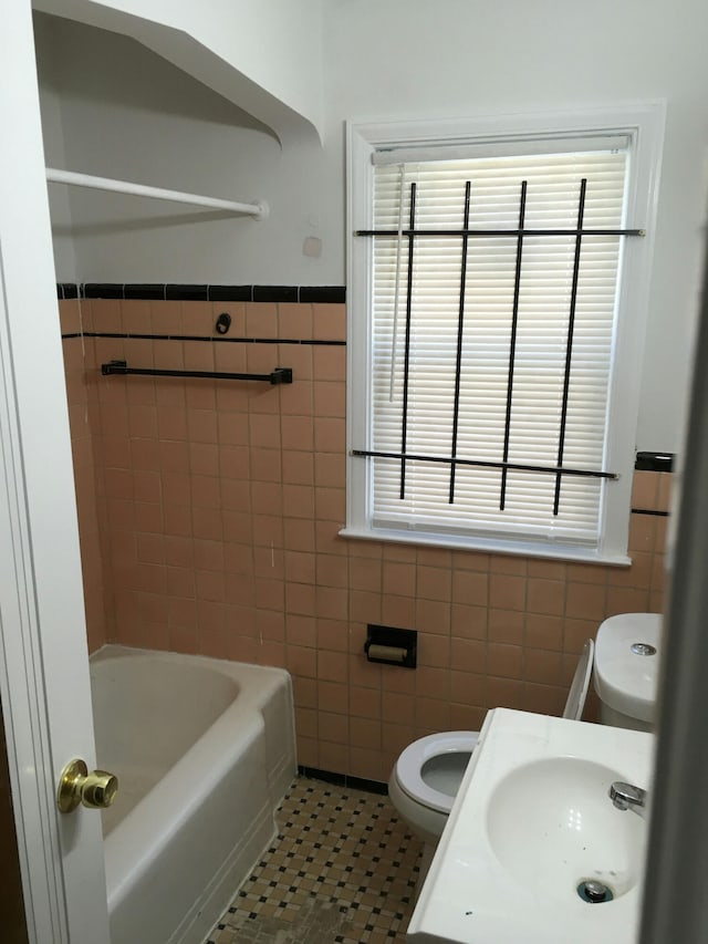 bathroom with tile patterned floors, toilet, sink, tile walls, and a bathing tub