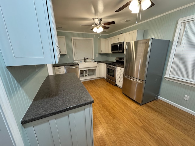 kitchen featuring appliances with stainless steel finishes, sink, white cabinets, ornamental molding, and light hardwood / wood-style floors