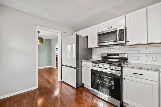 kitchen with white cabinetry, light stone counters, appliances with stainless steel finishes, dark hardwood / wood-style flooring, and backsplash